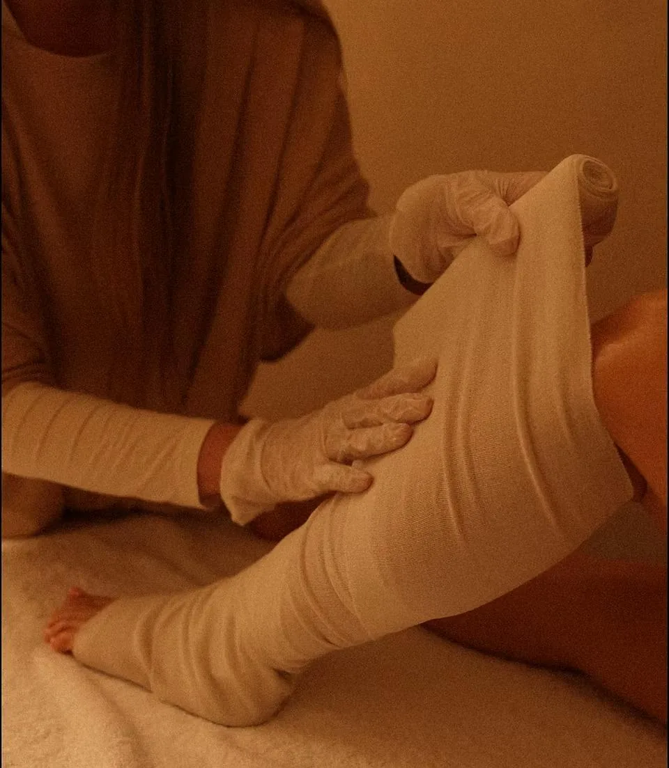 Therapist in gloves wrapping a client’s leg in an herbal-soaked bandage during a STYX body wrap